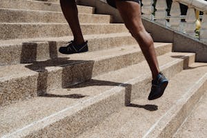 Close-up of a runner's legs ascending stone steps, capturing movement and shadow play.