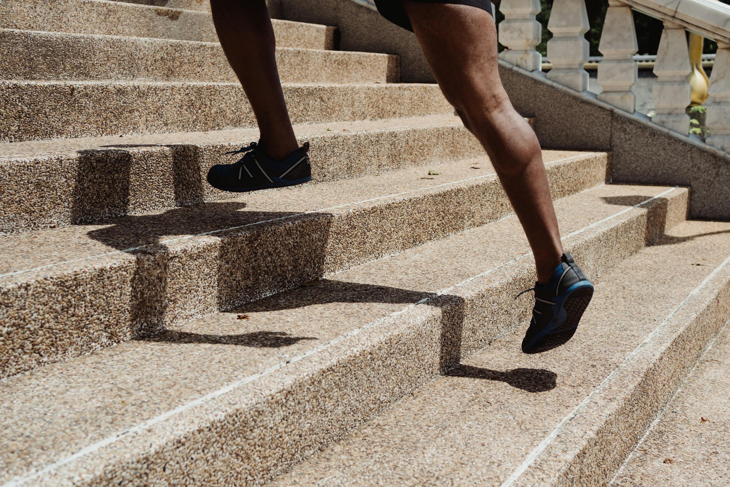 Close-up of a runner's legs ascending stone steps, capturing movement and shadow play.