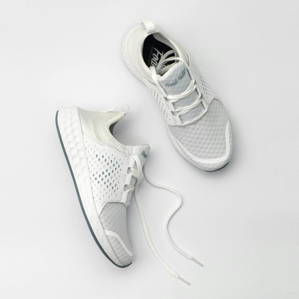 Pair of modern white sneakers with laces on a neutral backdrop.